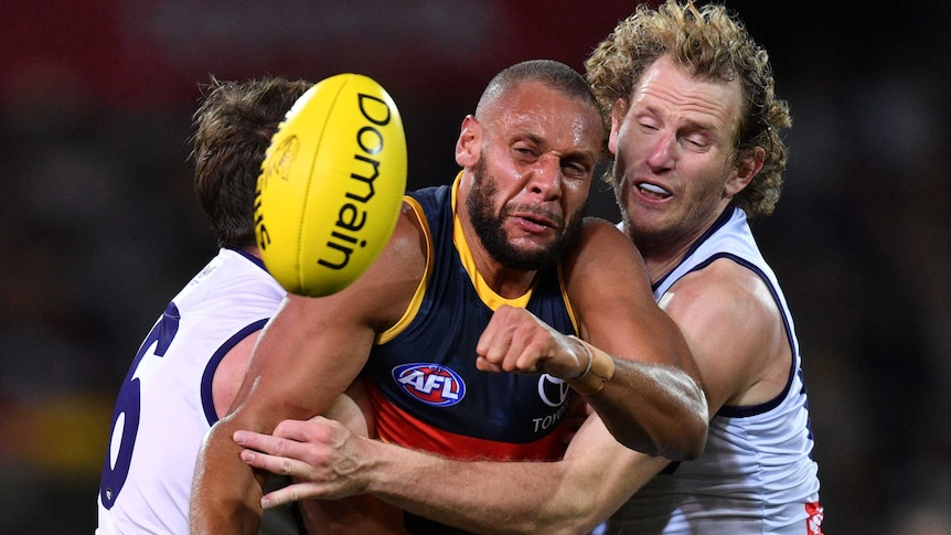 Cameron Ellis-Yolmen looks at the ball in front of him while standing in the middle of a two-man tackle against the Dockers.