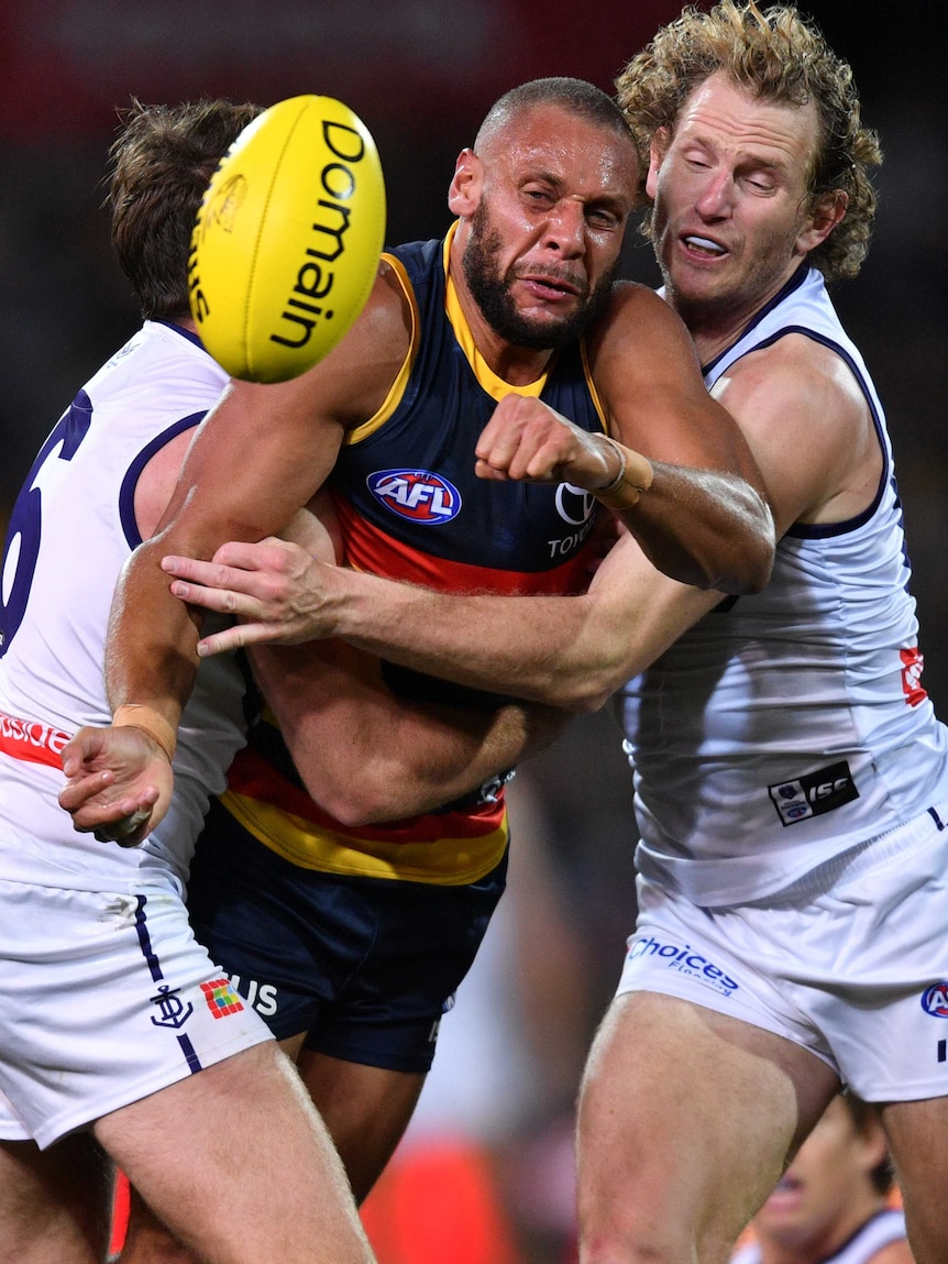 Cameron Ellis-Yolmen looks at the ball in front of him while standing in the middle of a two-man tackle against the Dockers.