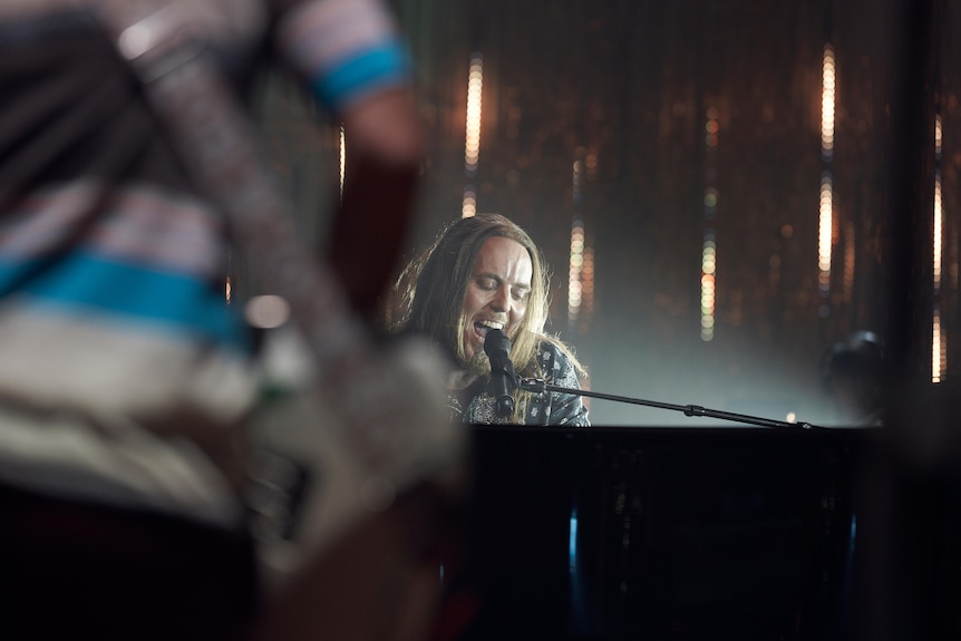 A man sings into a microphone while playing piano.