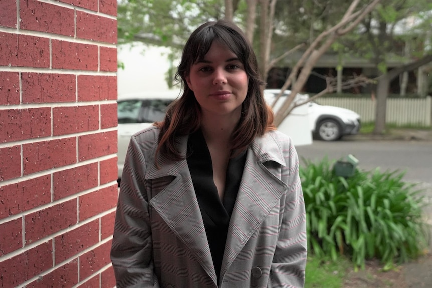 A woman wearing a beige jacket standing next to a brick wall outside