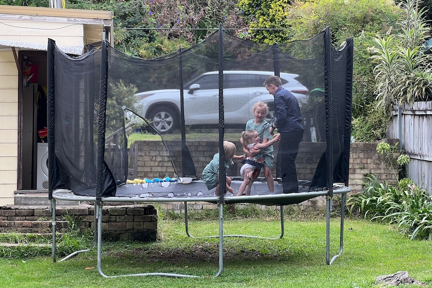 a group of three young children playing with a person on a trampoline