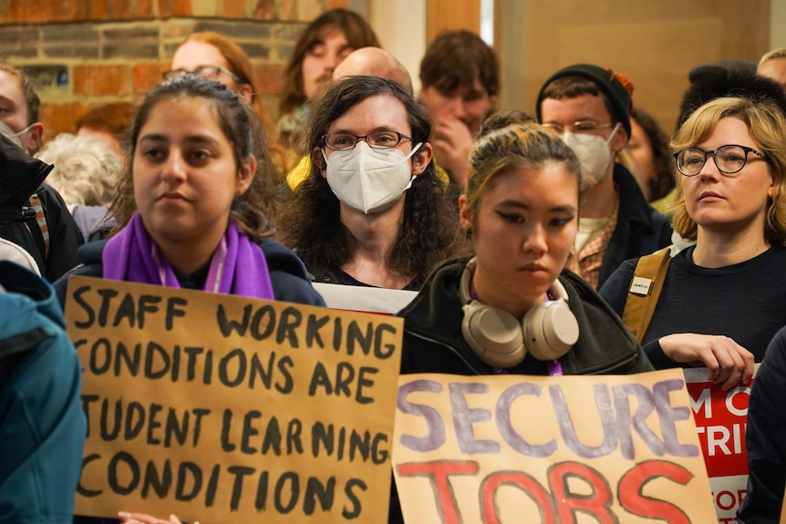 Grady in a crowd, between two women holding signs that read "staff working conditions are student learning conditions".
