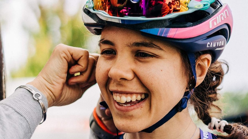Jess Pratt smiles widely as hands connect her helmet straps