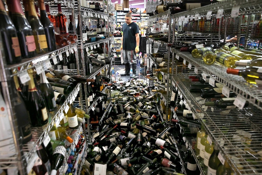 A worker looks at a pile of wine bottles that were thrown from the shelves in a liquor store during the earthquake.