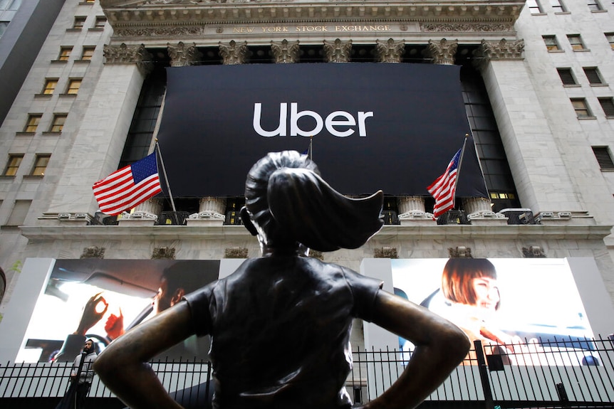 A photo of the Fearless Girl statue facing an Uber logo on the New York Stock Exchange building.
