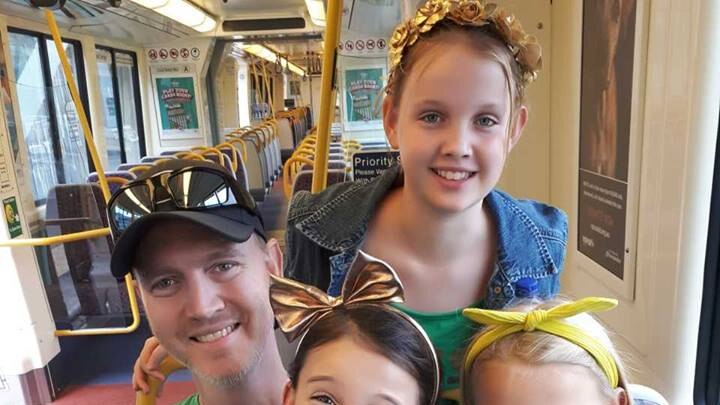 Man sits with his three young girls on light rail