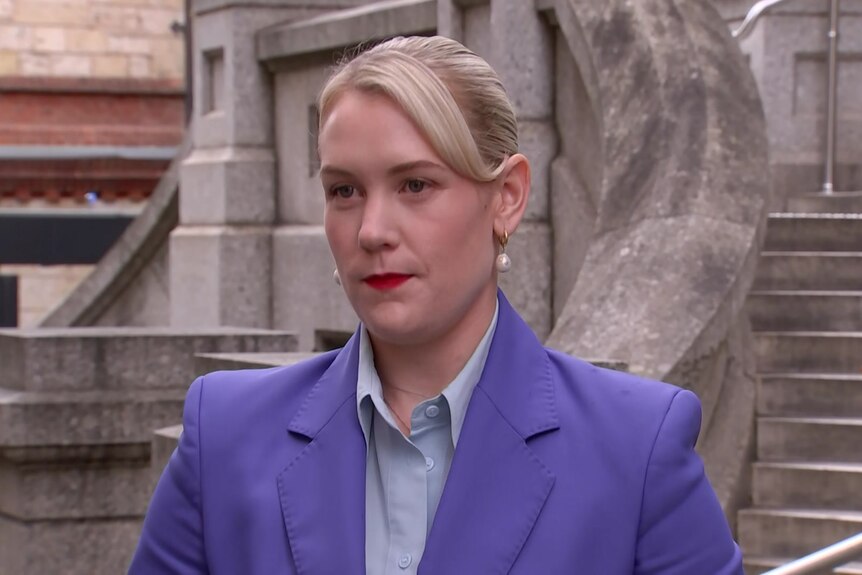 A blond woman in a purple suit outside steps of parliament house