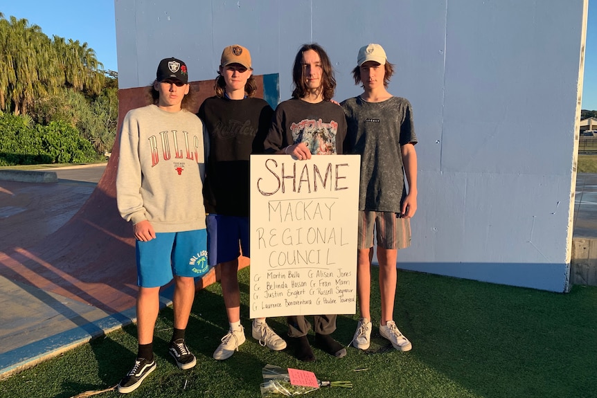 Four teenage boys hold up a sign that says 'Shame Mackay Regional Council'.