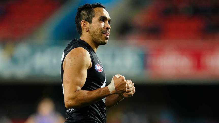 An Indigenous AFL footballer pumps his fists and smiles after kicking the final goal of the game.