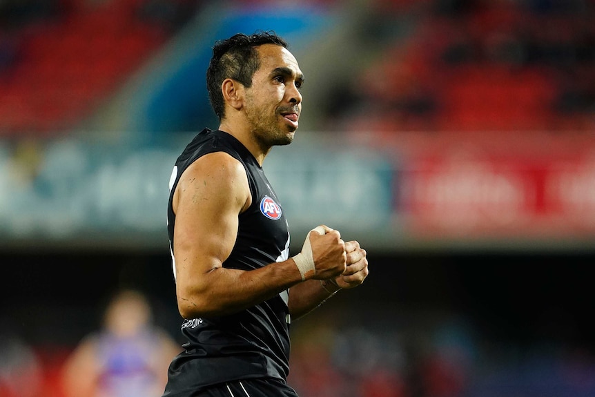 An Indigenous AFL footballer pumps his fists and smiles after kicking the final goal of the game.