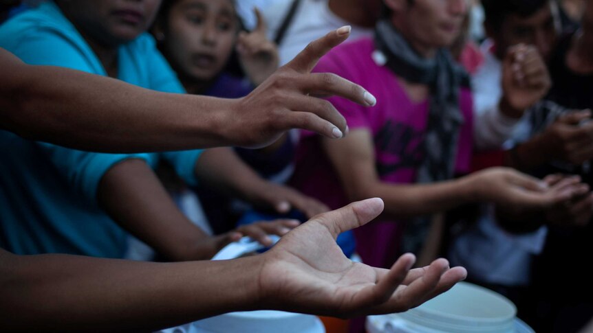 Migrants hold their hands out for food donations in Tapachula