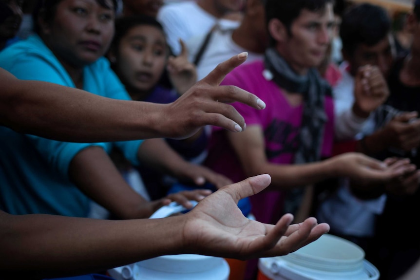 Migrants hold their hands out for food donations in Tapachula