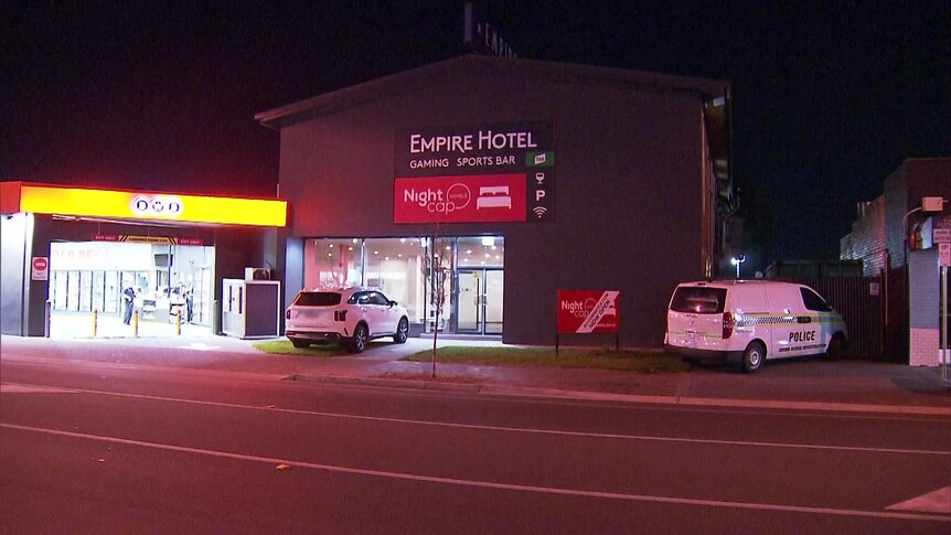 The front of a hotel with a sign reading Empire Hotel, with a BWS bottle shop to the left and a police car parked in front