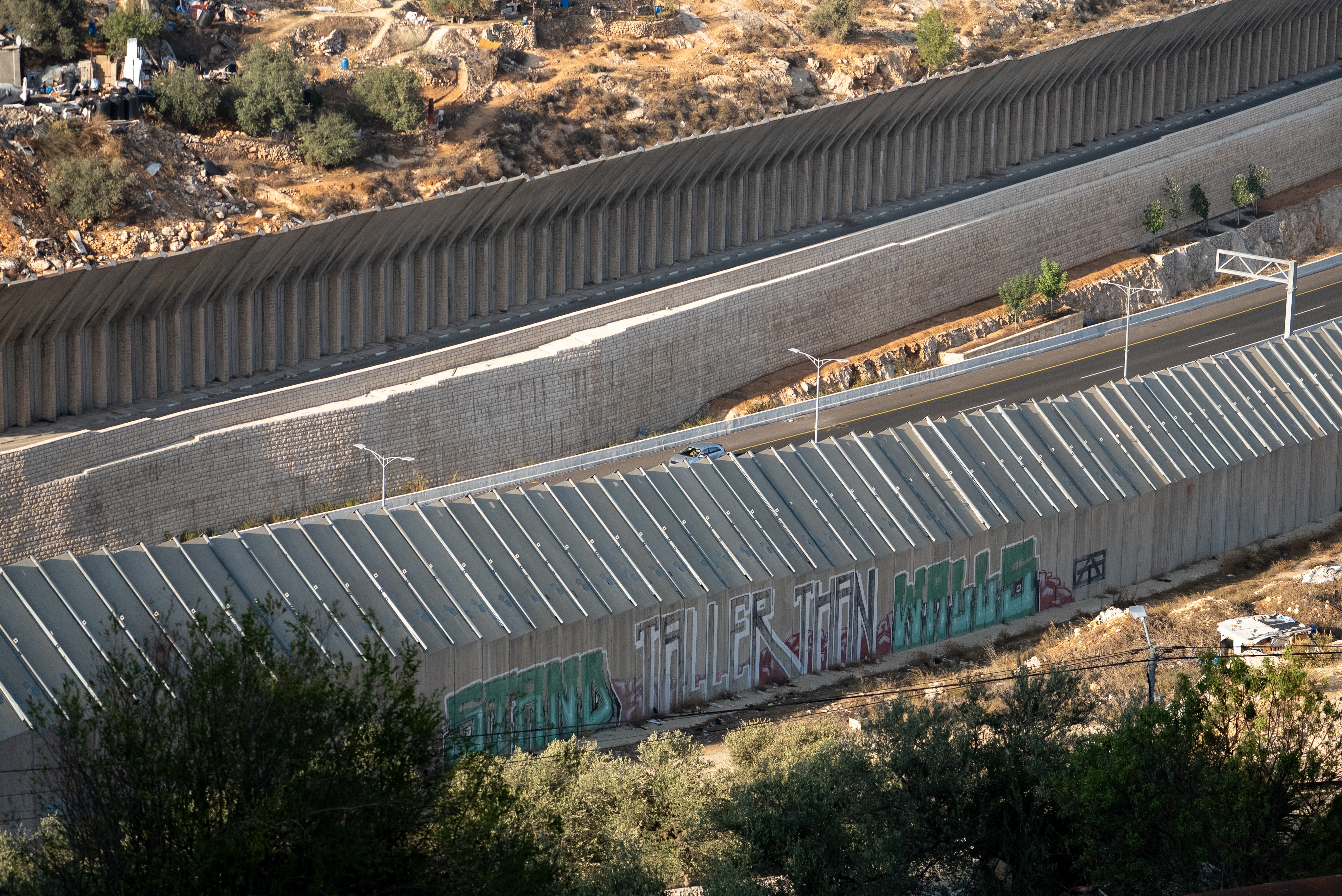 Tall concrete walls stretching along arid land with a street running between them