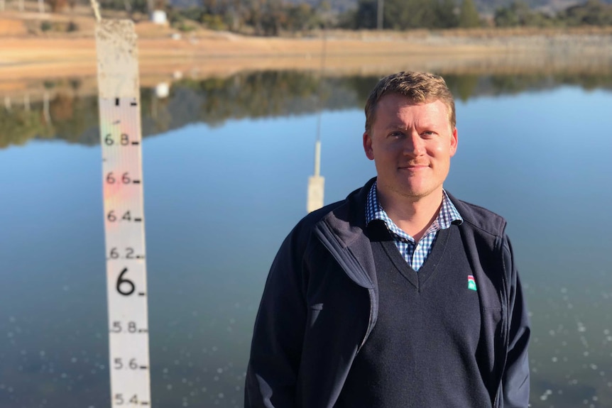 Man stands in front of water, well below a water marker next to him which has a height of 7 metres.