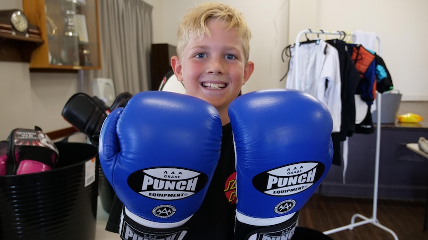 A young boy wearing new, blue boxing gloves smiles