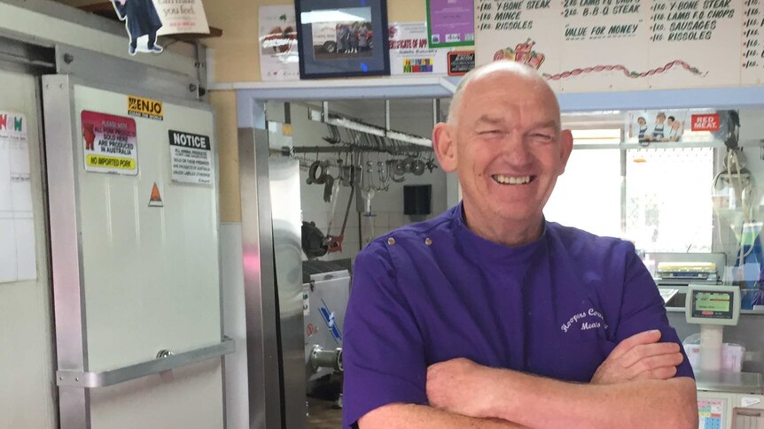 Glen Innes butcher Terry Hooper standing behind his shop's counter, smiling and with arms folded.