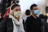 A person in a lemon-patterned face mask walks towards a tram.