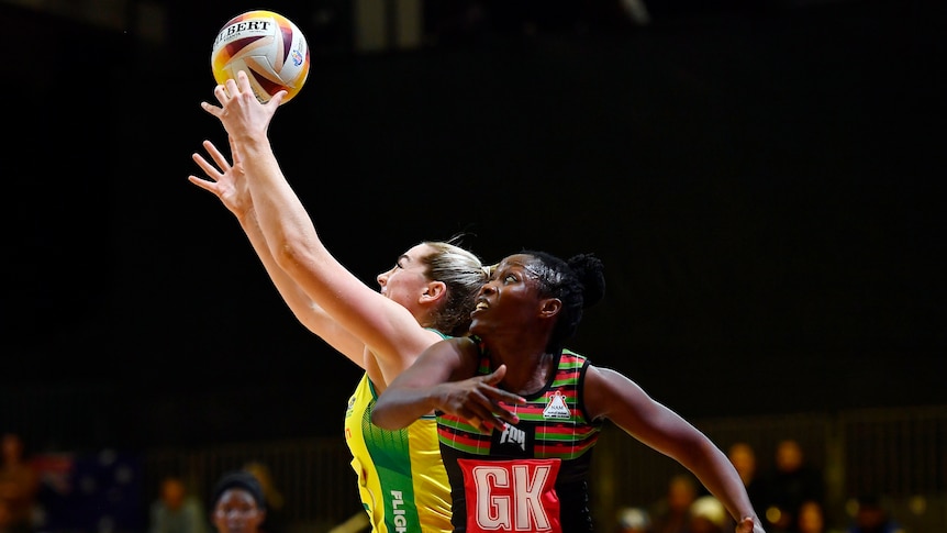 An Australian netballer reaches up to grab the ball as a Malawi player looks up.
