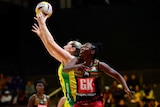An Australian netballer reaches up to grab the ball as a Malawi player looks up.