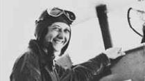 Historical black and white photo of Lores Bonney in her aviator outfit standing beside a plane, date unknown