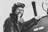 Historical black and white photo of Lores Bonney in her aviator outfit standing beside a plane, date unknown