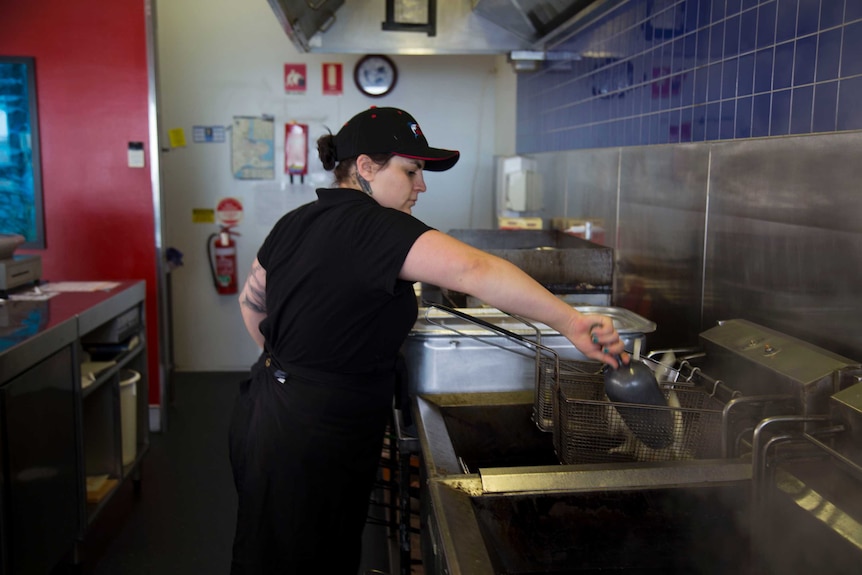 A young woman places chips in a commercial fryer.