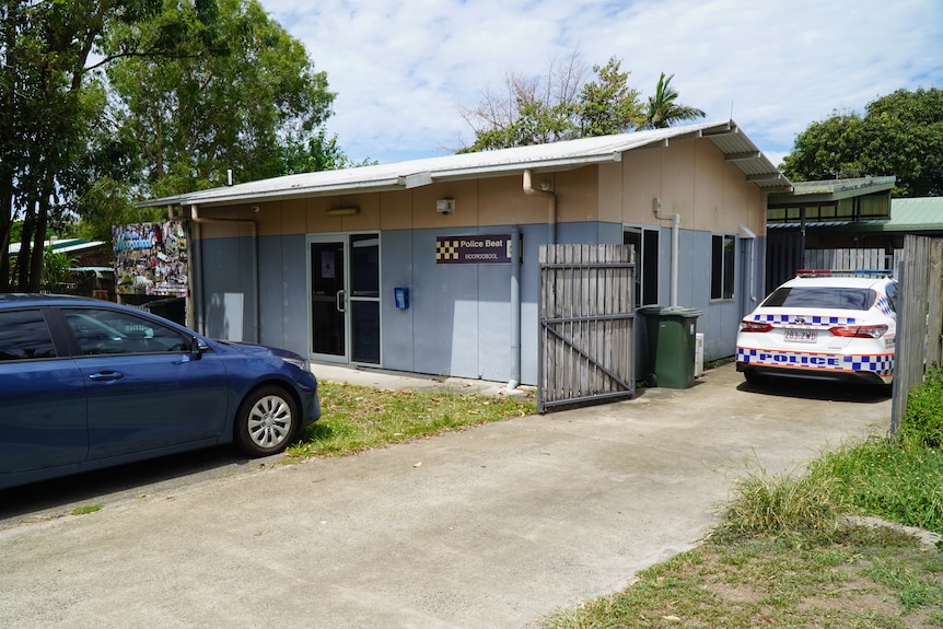 A small, blue police building next to a park, several cars outside