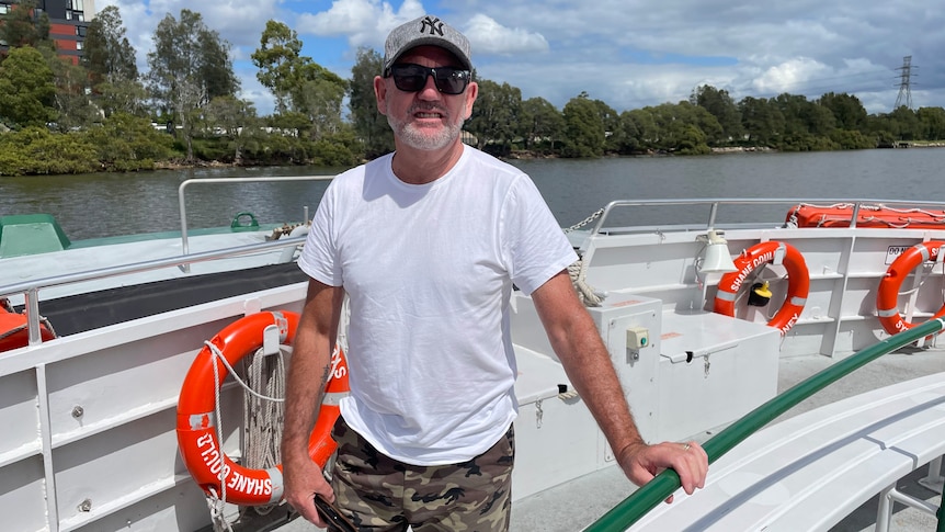 Man in white shirt and hat standing on boat in front of life saver rings.