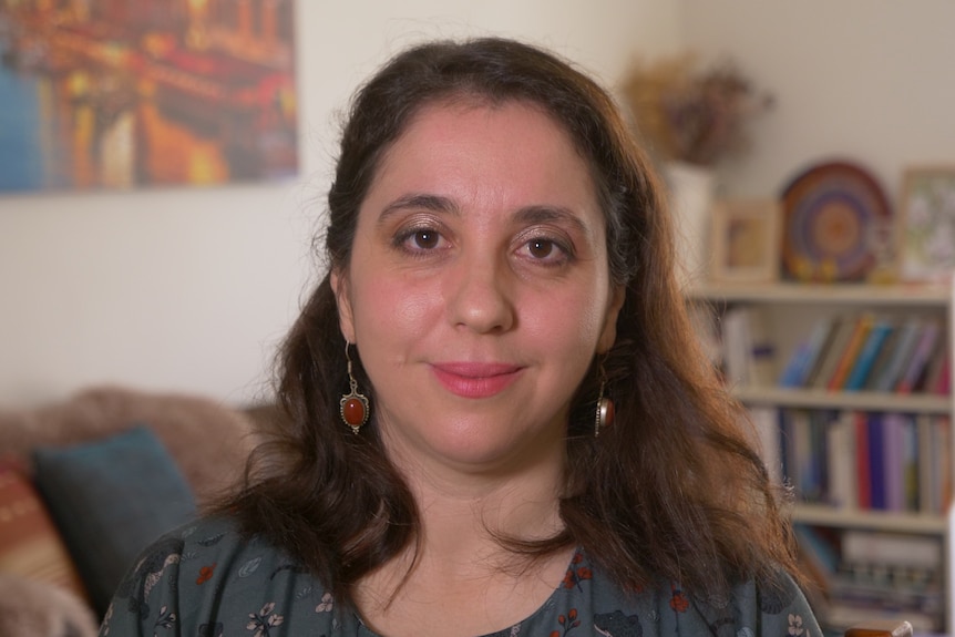 A woman with dark hair looks into the camera with a serious expression. 