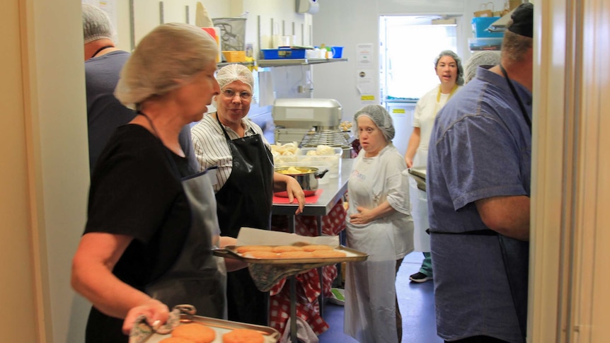 People with hairnets and aprons in a small and busy kitchen