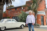 Woman standing and smiling outside a red brick pub named "Railway Hotel" with vintage car in background. 