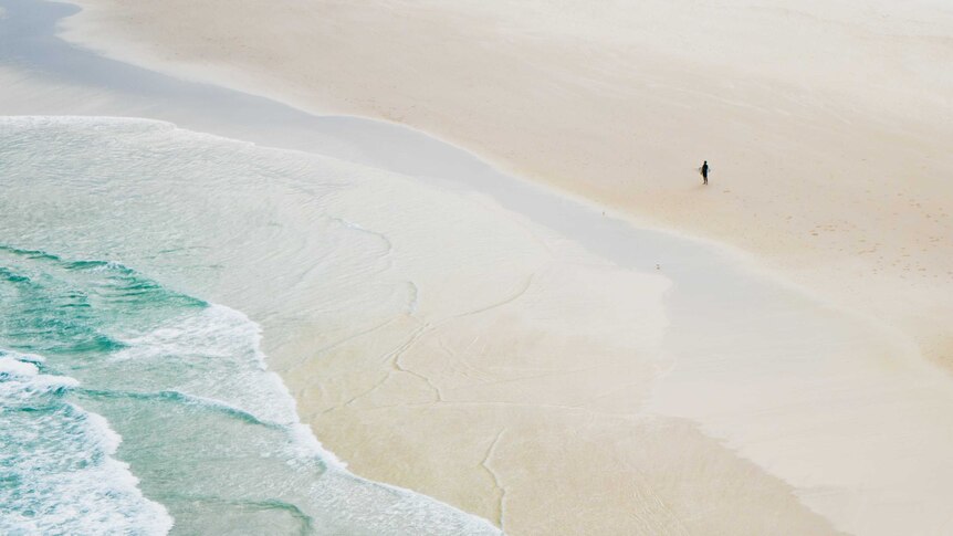 A man is dwarfed by the vastness of Tallow Beach at Byron Bay.