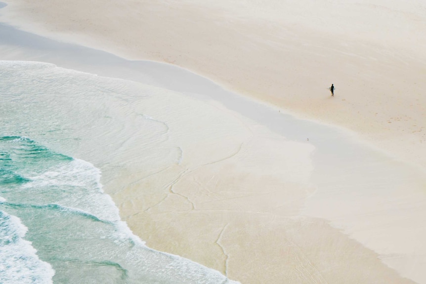 A man is dwarfed by the vastness of Tallow Beach at Byron Bay.