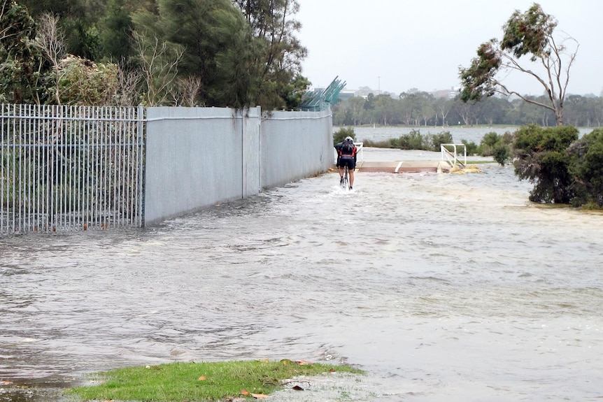 Cyclist rides along flooded bike path next to the Swan River in Perth.