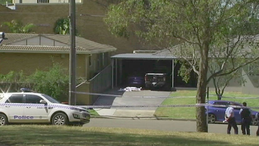 The man's body covered by a white sheet on a driveway outside a suburban home.