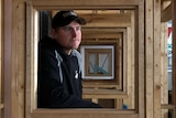 A man sits in a wooden frame and looks into the distance