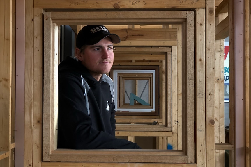 A man sits in a wooden frame and looks into the distance