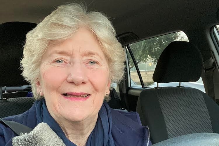 an elderly woman smiles in a selfie taken in the front seat of a car