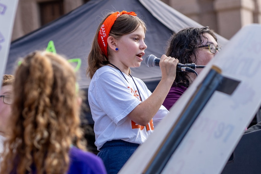 Young girl holding a microphone speaking at a protest.