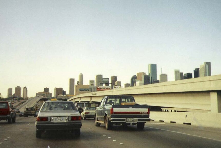 An old photo of cars driving down a major freeway with the Houston skyline in the background 