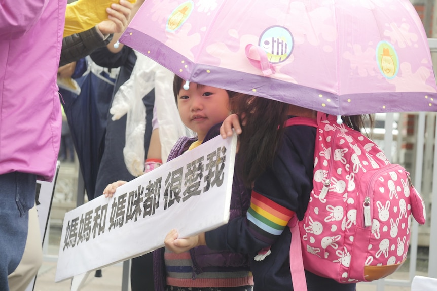 A Taiwanese child holds a sign reading, "Both mum and mummy love me very much".