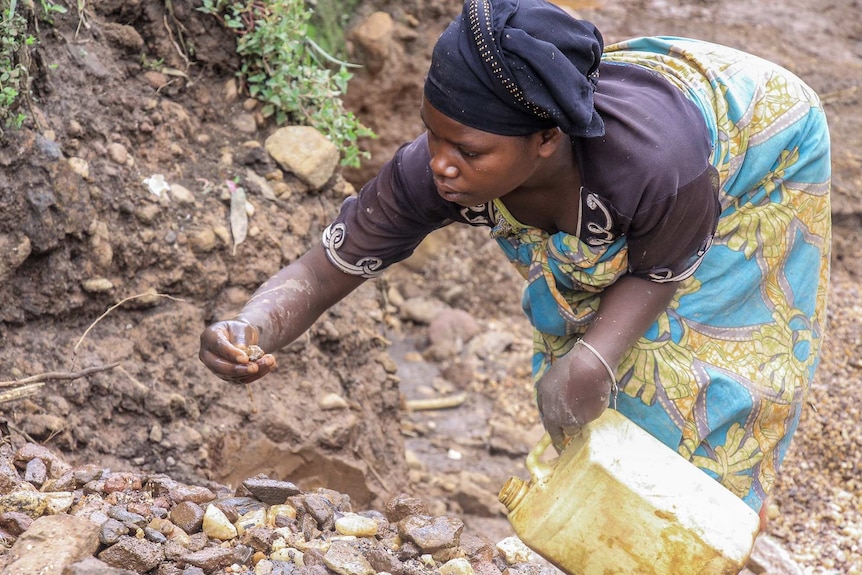 A woman bends down and picks up stones.