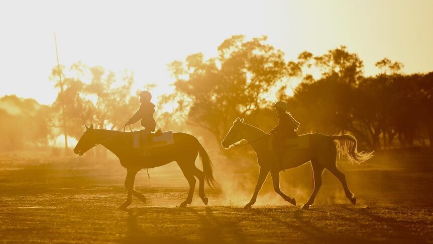 Two children ride their ponies along a dusty road, with the sun rising behind them.
