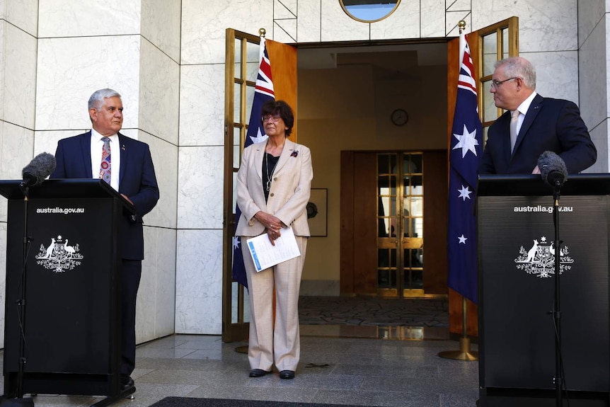 Ken Wyatt and Scott Morrison stand at separate, spaced out podiums. Pat Turner is between them.