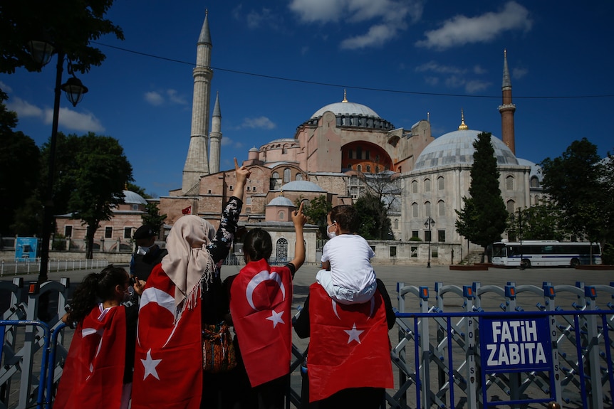 People draped in Turkish flags stand outside the Hagia Sophia.