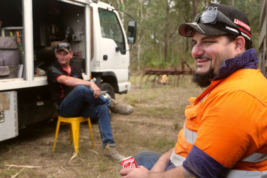 two men sit around having a drink, smiling off in the distance 