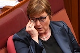 Linda Reynolds wipes her eye under her glasses with a tissue while sitting in the Senate chamber