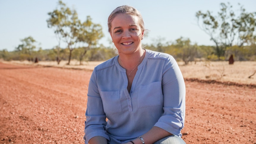 Janessa Bidgood, a young woman who grew up in the west and moved back, squats on a red dirt road near Cloncurry.
