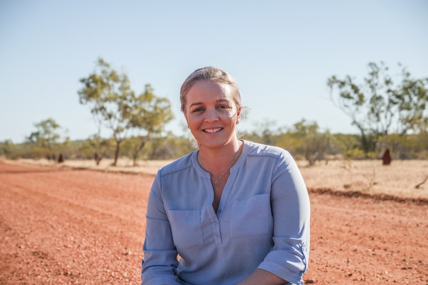 Janessa Bidgood, a young woman who grew up in the west and moved back, squats on a red dirt road near Cloncurry.